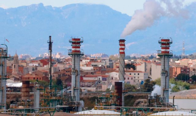 Xemeneies de la indústria química de Tarragona fumejant en primer terme i, al fons, habitatges dels pobles del Morell i la Pobla de Mafumet, al Tarragonès