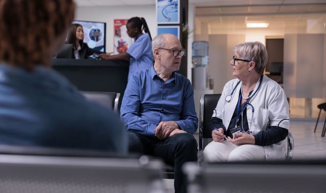 Un médico consultando con un paciente en la sala de espera de un hospital | iStock