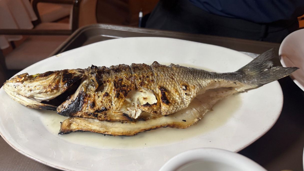 Preparació del llobarro a la brasa a taula, servida amb aigua de Lourdes, al restaurant Adobo Barcelona | ACN Preparació del llobarro a la brasa a taula, servida amb aigua de Lourdes, al restaurant Adobo Barcelona | ACN