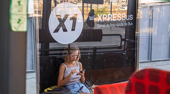 Una chica consultando el móvil en una parada de la línea X1 | TMB Una chica consultando el móvil en una parada de la línea X1 | TMB