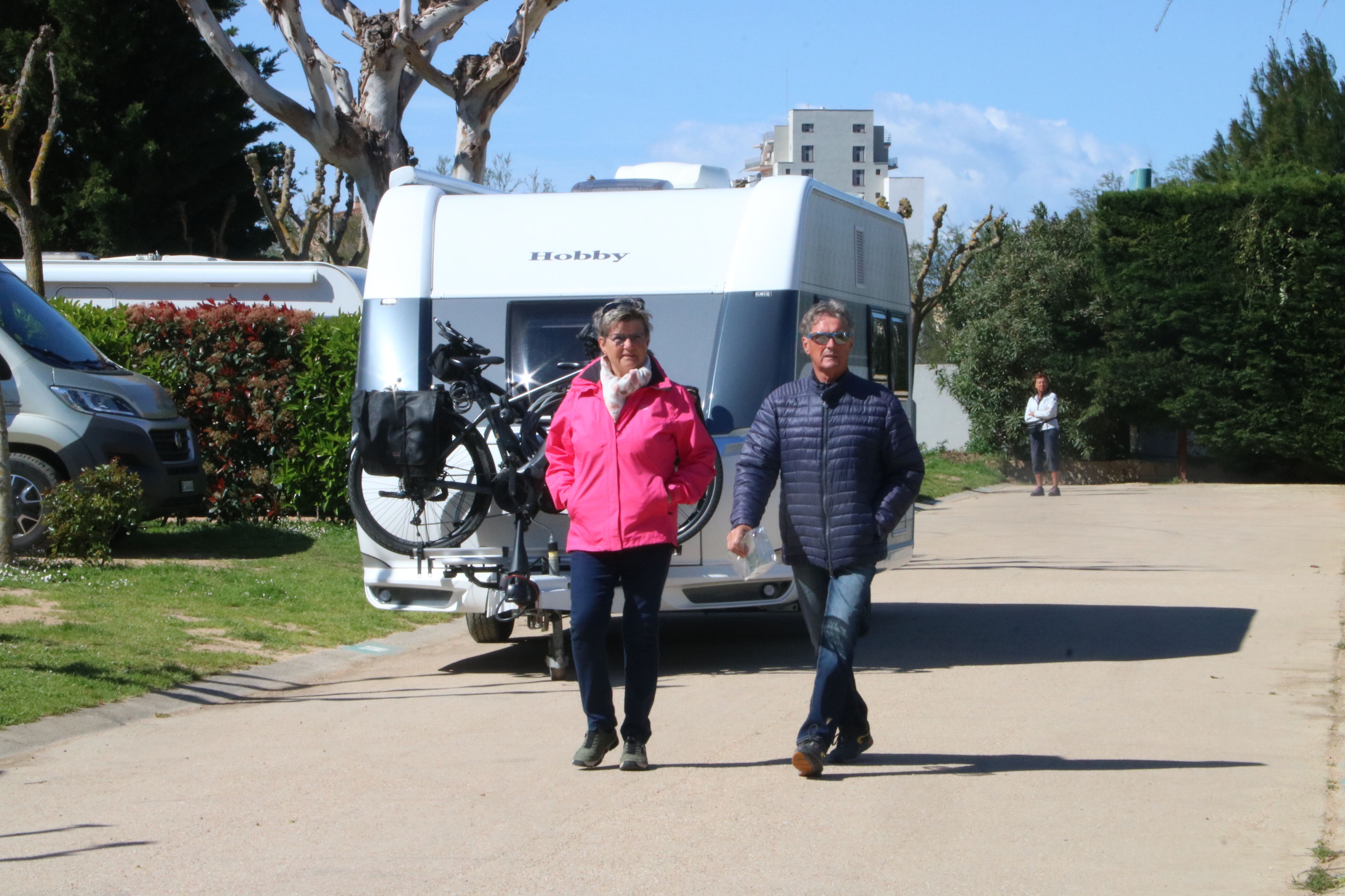 Dues persones passejant pel càmping Salatà de Roses amb una caravana al darrere | ACN