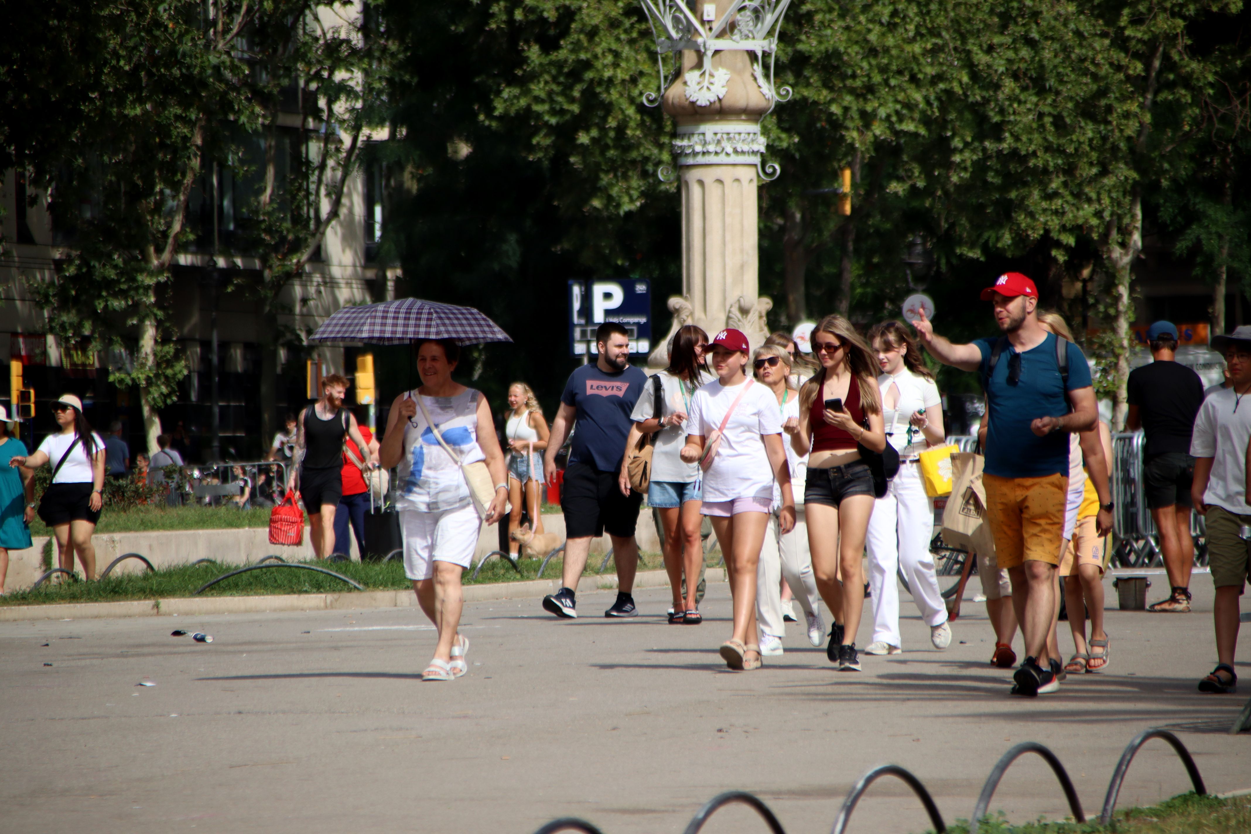 Persones passegen pel passeig Lluís Companys amb gorres i un paraigua | Blanca Blay (ACN)