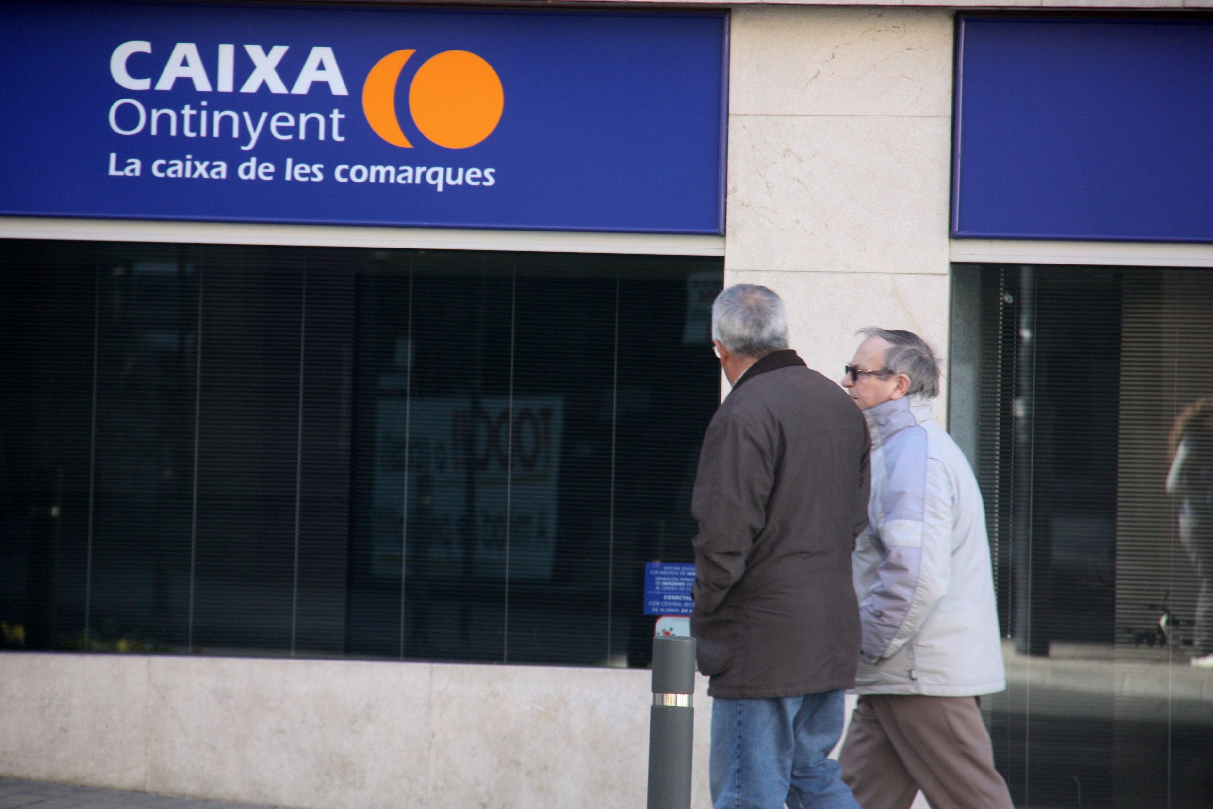 Dos persones passen per davant d'una oficina de Caixa Ontinyent a Ontinyent | ACN Dos persones passen per davant d'una oficina de Caixa Ontinyent a Ontinyent | ACN